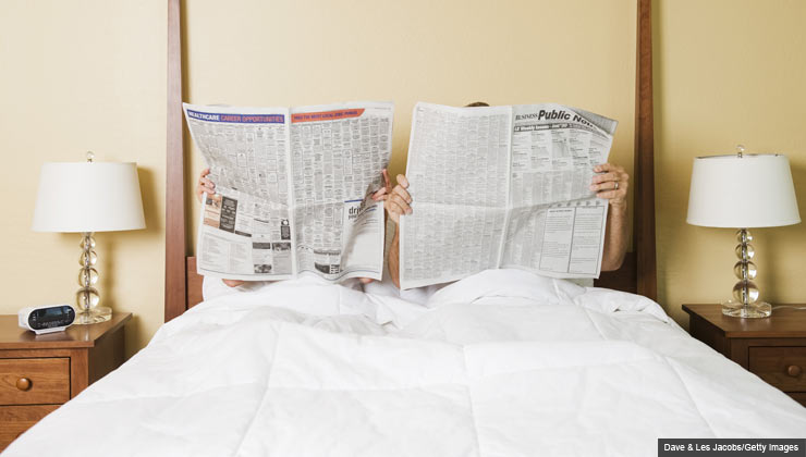 زن و مرد روی تخت در حال خواندن روزنامه